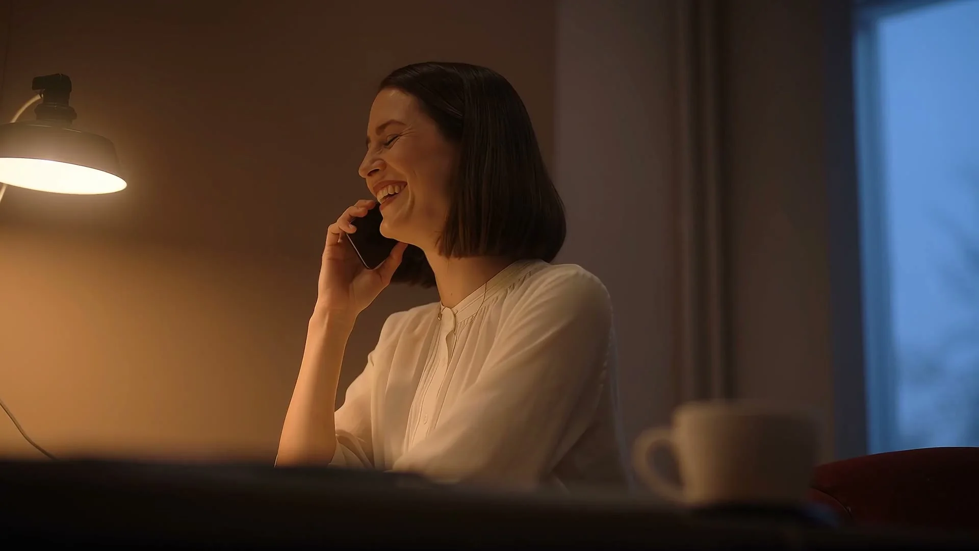 A renter laughing on the phone in a lamp-lit room in the evening